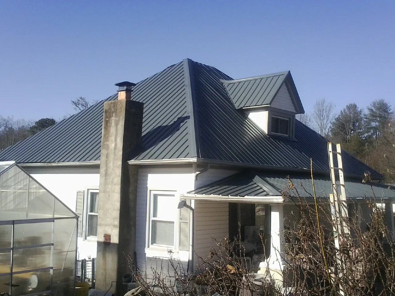 Dark blue standing seam metal roof on a white farmhouse with dormer — Slate & Tile Roof Repair by Roofing Brothers in Eckert