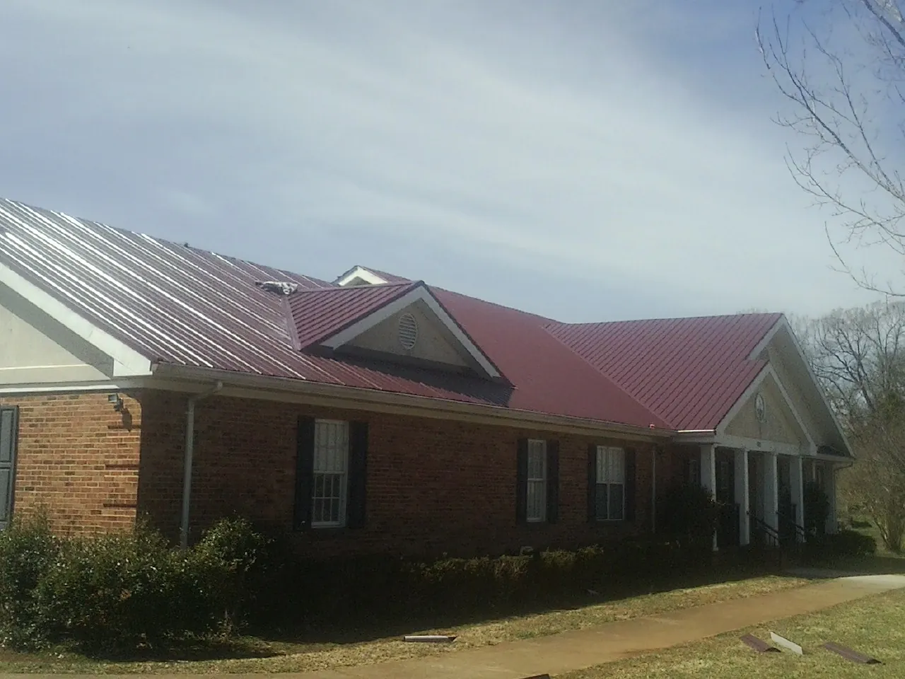 Red metal roof with gabled entries on a long brick building, from a Hail Damage Roof Repair job in Eckert
