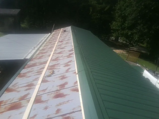 Old rusted panels beside newly installed green metal roofing — Wind Damage Roof Repair by Roofing Brothers in Eckert