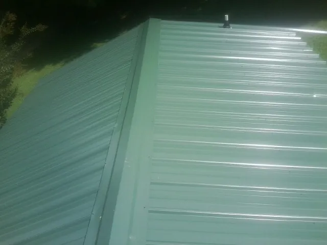 New green metal panels meeting at the ridge of a roof — Flat Roof Repair work by our crew in Eckert