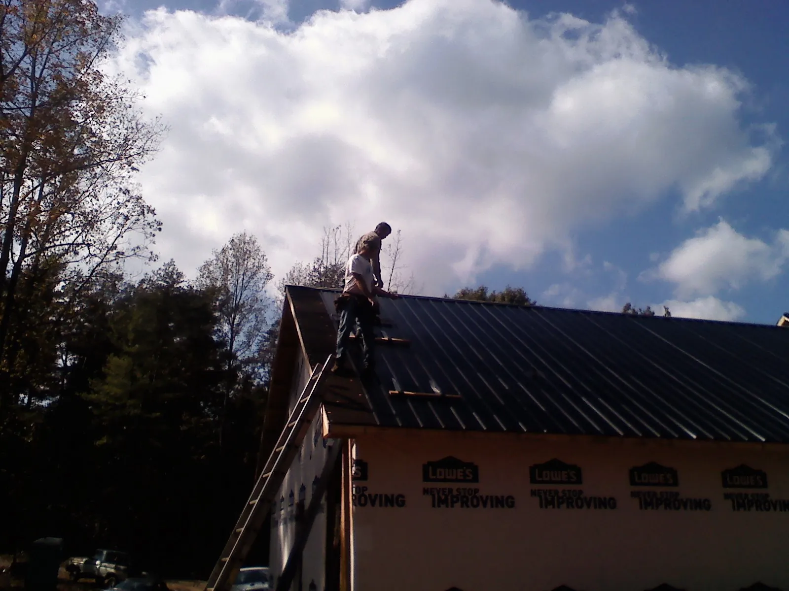 Roofer fastening dark metal panels high against a cloudy sky, from a Roof Inspection job in Eckert
